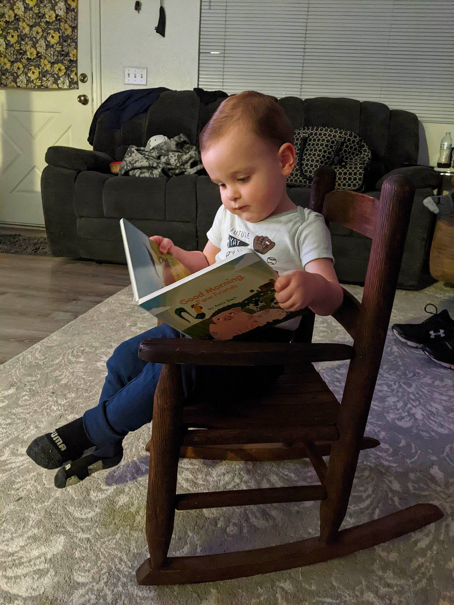 Mitchell is registered to the contest to win money with this photo: baby, chair, child, comfort, couch, flooring, furniture, houseplant, lamp, lap, leg, living_room, person, picture_frame, plant, reading, room, shoe, sitting, sneakers