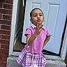 accessory, brick_wall, child, concrete, cute, door, fashion, girl, outdoor, person, pink_shirt, pink_shoes, plaid_skirt, playful, pose, sidewalk, standing, unicorn_purse, white_socks, young