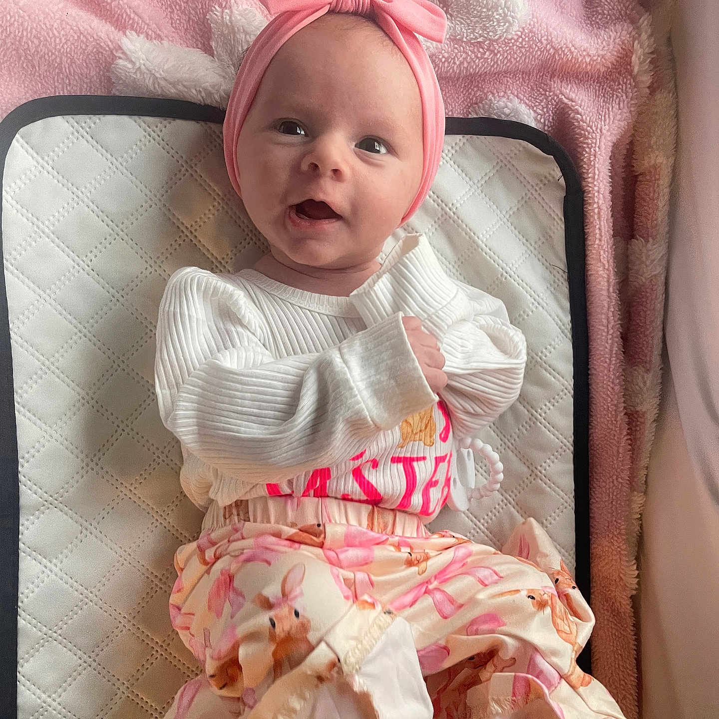 Lakelynn Rylie joined the competition — help win amazing prizes! baby, child, infant, portrait, face, smiling, indoors, pink, headband, bow, floral_clothing, dress, white_shirt, blanket, quilted_mat, lying_down, nursery, cute, seated, looking_at_camera
