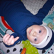 Theodore is registered to the contest to win money with this photo: baby, child, blue_clothing, beanie, blanket, colorful, pattern, indoor, infant, laying_down, pacifier, person, portrait, reaching_hand, red_eye, soft_toys, toy, white, young_child, cute