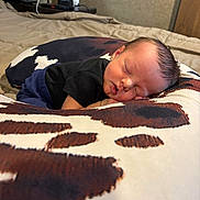 Stetson is registered to the contest to win money with this photo: baby, sleeping, newborn, pillow, cow_pattern, black_shirt, blue_pants, bedroom, bed, blanket, face, infant, resting, cute, peaceful, indoors, person, soft, young, head