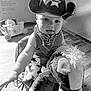 child, toddler, cowboy_hat, bandana, plush_toy, rocking_horse, indoor, wooden_floor, black_and_white, baby, toy, play, smiling, cute, person, infant, hat, costume, fun, portrait