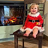 toddler, child, smiling, red_dress, santa_outfit, chair, wooden_floor, fireplace, christmas_decorations, toy, holiday, indoor, cute, happy, festive, home, decor, winter, seasonal, portrait