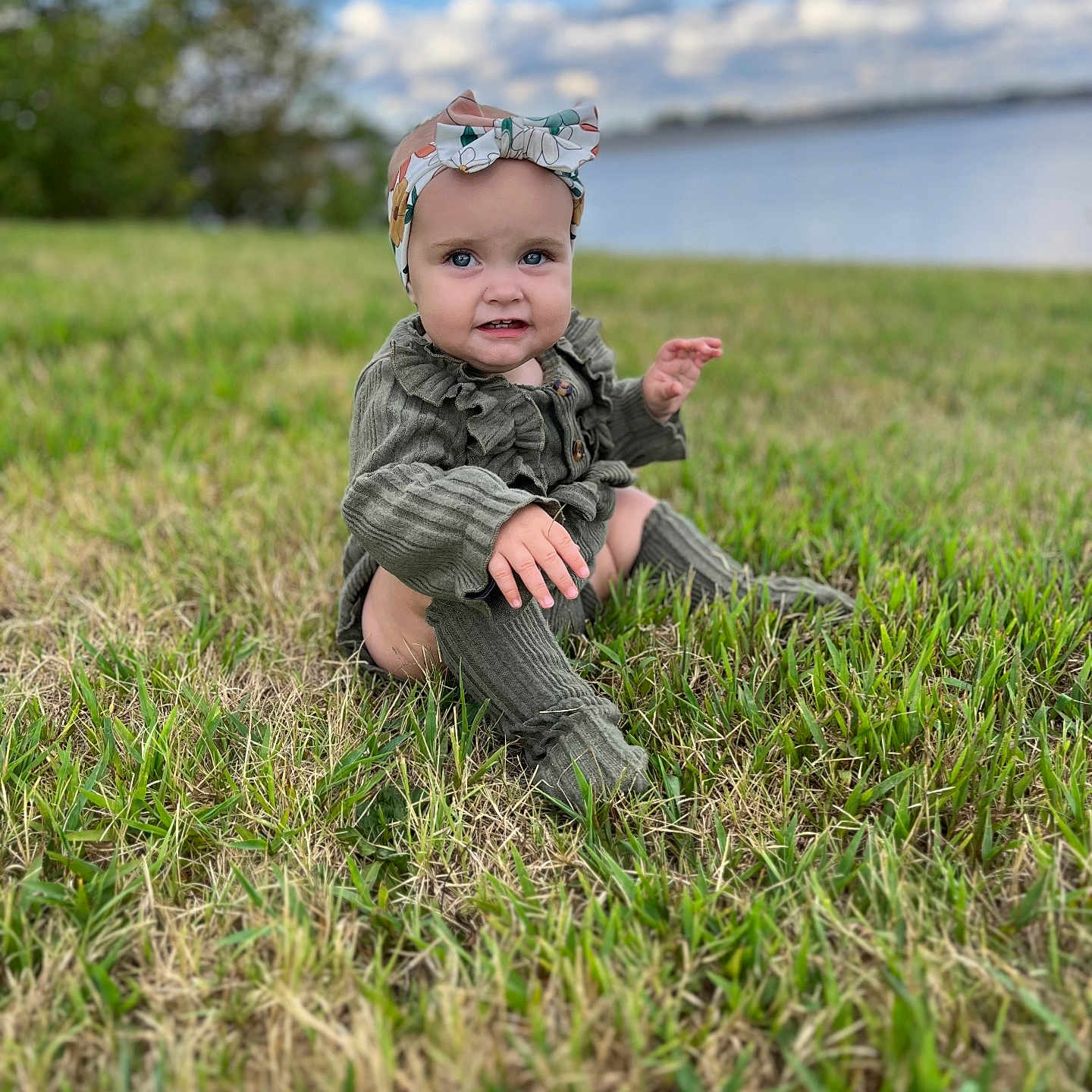Millie is registered to the contest to win money with this photo: baby, clothing, face, field, grass, grassland, head, lawn, nature, outdoors, pants, park, person, photography, plant, portrait, rock, sitting, tree, vegetation