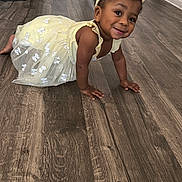 Nina is registered to the contest to win money with this photo: toddler, child, yellow_dress, headband, crawling, smiling, indoor, wooden_floor, happy, baby, person, cute, young_child, flooring, playful, small_child, head, skin_tone, hands, eyes