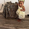 Nina is registered to the contest to win money with this photo: toddler, child, yellow_dress, headband, barefoot, leopard_print, fabric, wooden_floor, smile, indoor, wall, plug, electrical_outlet, person, curly_hair, cute, standing, playful, home, flooring