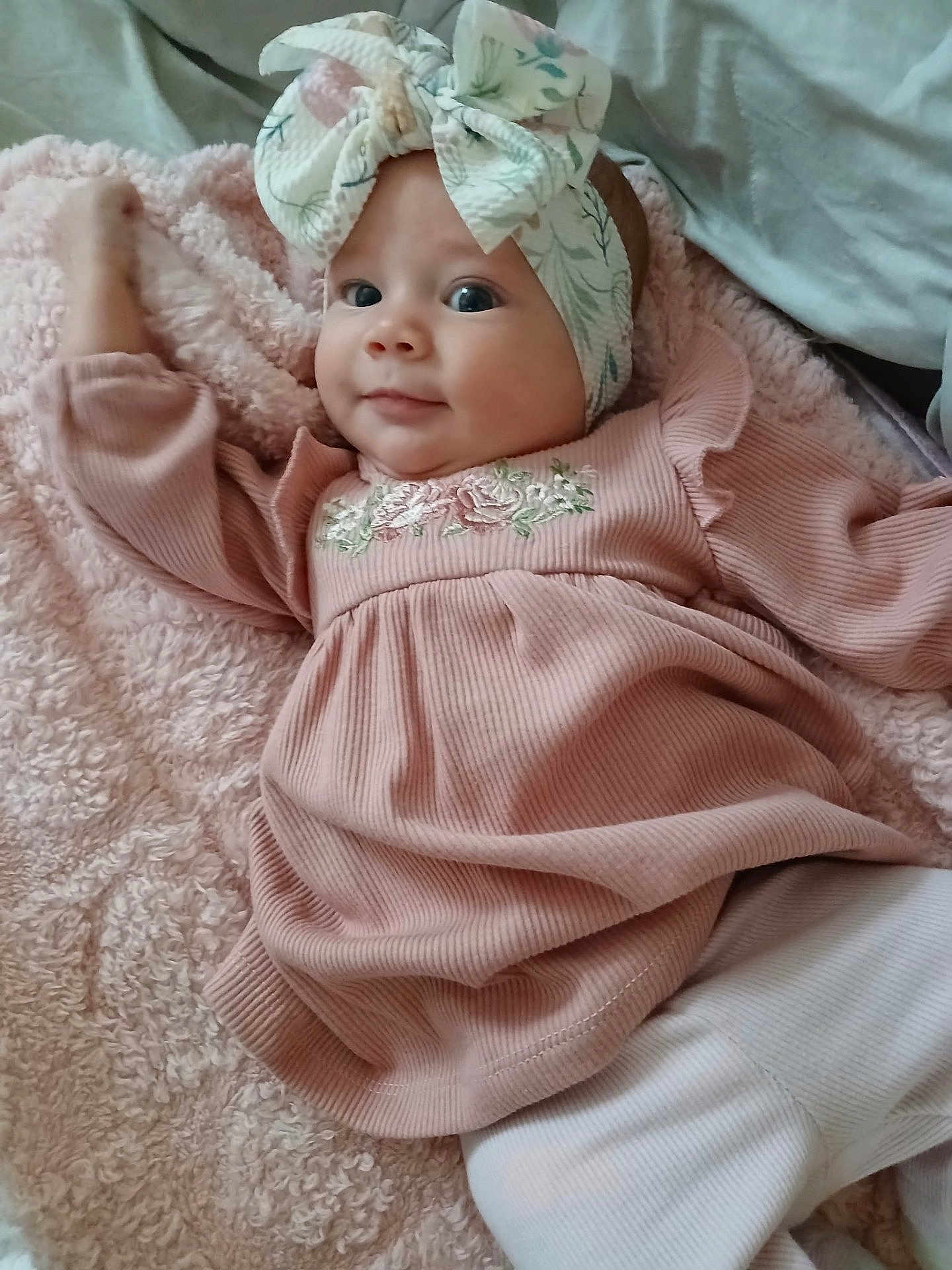 Alina is registered to the contest to win money with this photo: baby, infant, headband, pink_dress, blanket, smile, face, cute, child, lying_down, cozy, soft_texture, indoor, portrait, young_child, apparel, headwear, happy, closeup, person