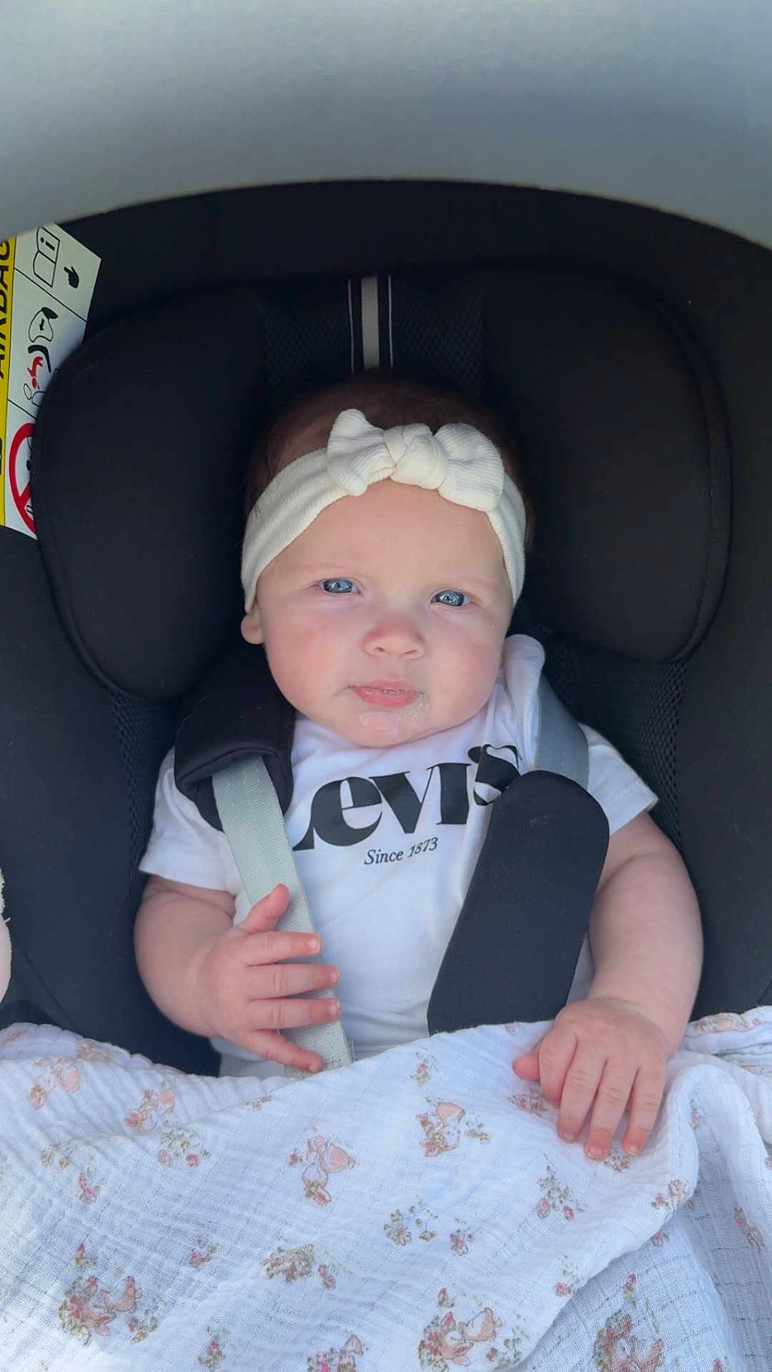 Victoire participe au concours pour gagner de l'argent avec cette photo : baby, infant, car_seat, headband, blue_eyes, white_shirt, blanket, floral_pattern, hands, face, child, cute, seatbelt, portrait, indoor, person, clothing, baby_girl, closeup, expression