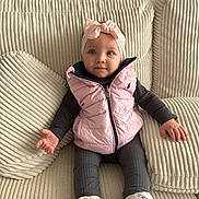 Victoire a rejoint le concours — aidez-le/la à gagner de superbes lots ! baby, blue_eyes, child, clothing, couch, cozy, cute, expression, footwear, hands, headband, indoor, infant, pillows, pink_bow, pink_vest, portrait, seated, textured_fabric, white_sneakers