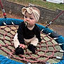 baby, child, pacifier, headband, rope_swing, playground, outdoor, grass, rope, black_clothing, beige_clothing, socks, seat, curious, sitting, person, toy, fence, van, side_view