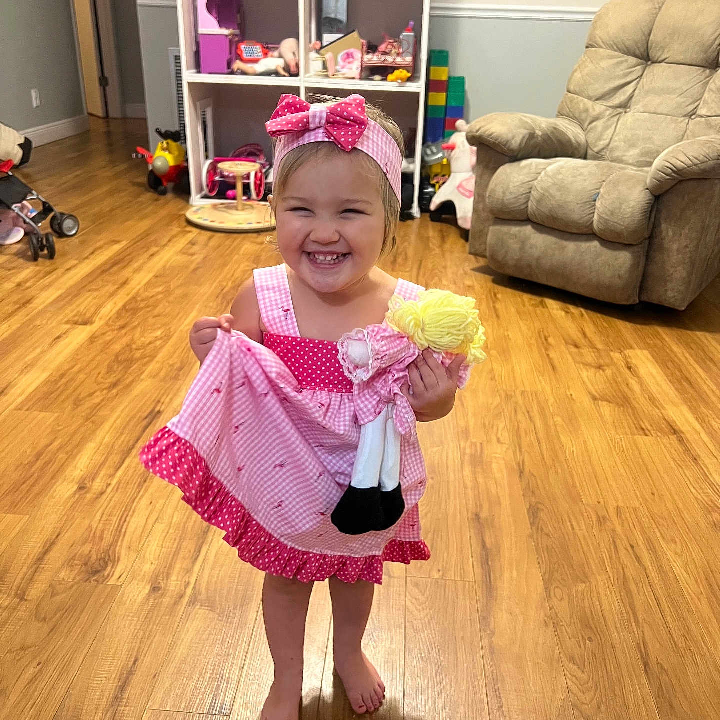 Drue joined the competition — help win amazing prizes! armchair, barefoot, child, cute, doll, furniture, girl, happy, headband, home, indoors, living_room, person, pink_dress, play, smiling, toddler, toys, wooden_floor, young_child