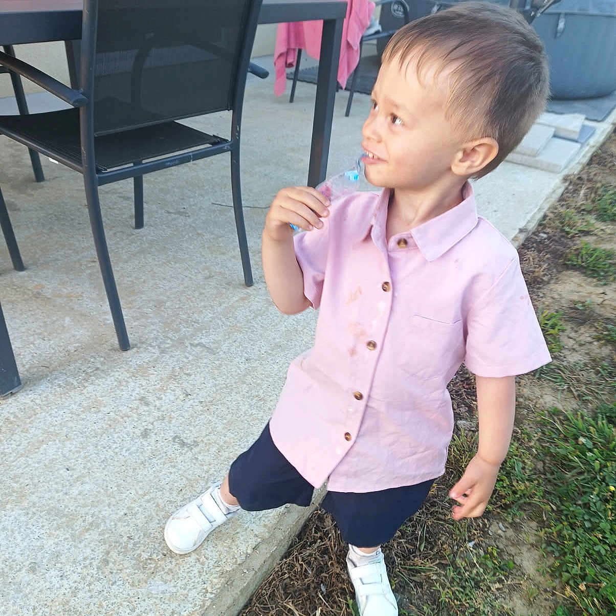 Timaé joined the competition — help win amazing prizes! toddler, child, boy, pink_shirt, shorts, white_shoes, outdoor, patio, table, chairs, grass, concrete, curious_expression, daylight, side_view, holding_object, messy_shirt, casual, person, small_child