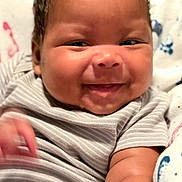 Domani is registered to the contest to win money with this photo: baby, infant, smile, face, cheeks, onesie, striped_clothing, arm, skin, blanket, pattern, happy, cute, child, portrait, closeup, indoors, person, newborn, young_child