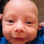 Theo joined the competition — help win amazing prizes! baby, close_up, face, infant, blue_clothing, star_pattern, skin, head, eyes, nose, mouth, hand, fingers, texture, background, indoor, portrait, cute, child, young