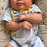 baby, infant, child, cute, smiling, lying_down, cushion, floral_pattern, clothing, yellow_socks, cartoon_characters, bow_tie, suspenders, indoors, portrait, skin, face, hands, feet, happy