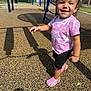 toddler, child, smiling, playground, outdoor, sunny, pink_shoes, tie_dye_shirt, black_shorts, shadow, happy, person, recreation, daylight, play_equipment, fence, trees, grass, urban, park