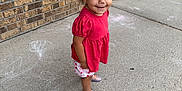 Ella joined the competition — help win amazing prizes! toddler, child, outdoor, sidewalk, chalk_drawings, brick_wall, red_top, patterned_shorts, shoes, curly_hair, smiling, standing, concrete, planter, window, casual_clothing, young_child, daylight, playtime, earrings