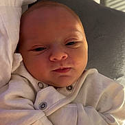 Noah is registered to the contest to win money with this photo: baby, infant, newborn, onesie, white_clothing, face, hand, cushion, blanket, sleepwear, closeup, person, indoors, skin, young_child, resting, soft_light, cute, peaceful, portrait