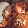 baby, infant, sleeping, smiling, blanket, clothing, winnie_the_pooh, sweater, couch, soft_lighting, indoor, cozy, resting, child, person, head, ear, fabric, comfort, cute