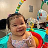 arm, baby, background, child, clothing, colorful, cute, face, furniture, hair_clip, hand, happy, indoor, infant, person, play_seat, plush_toy, rainbow, smile, toy