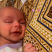 Wania is registered to the contest to win money with this photo: baby, infant, sleepy, smile, hand, pajamas, patterned_pillow, closeup, face, skin, cozy, cute, child, young, relaxing, indoor, person, comfort, resting, newborn