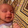 baby, infant, sleepy, smile, hand, pajamas, patterned_pillow, closeup, face, skin, cozy, cute, child, young, relaxing, indoor, person, comfort, resting, newborn