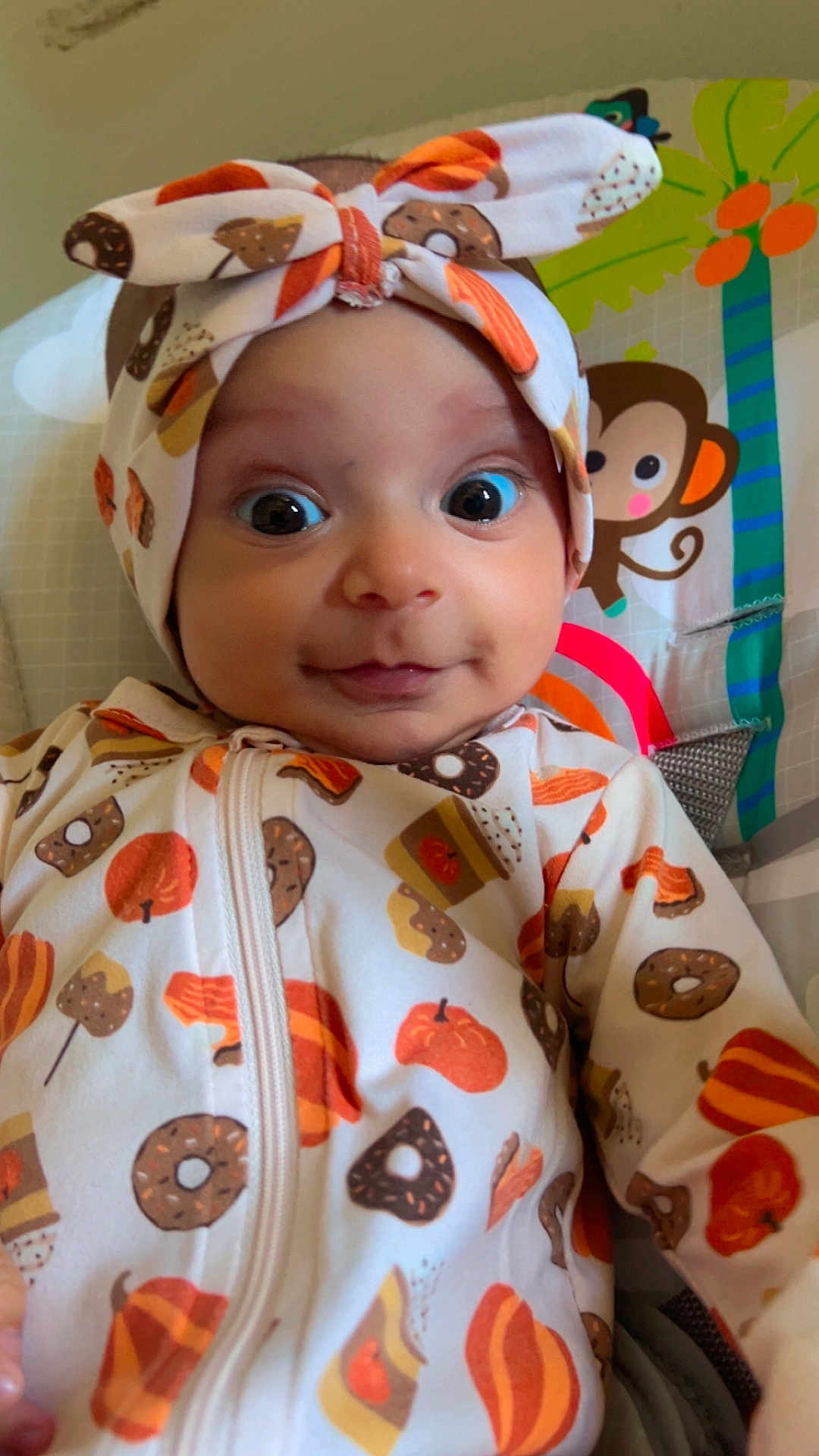 Wania is registered to the contest to win money with this photo: baby, infant, headband, onesie, pumpkin, donut, patterned_clothing, monkey, palm_tree, colorful, wide_eyes, cute, portrait, child, indoor, smiling, seated, playful, background, close_up
