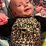 baby, smile, infant, clothing, leopard_print, text_on_clothing, blanket, polka_dot, pink, gray, cozy, cute, child, lying_down, happy, face, person, soft, warm, indoor