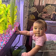 Amira joined the competition — help win amazing prizes! baby, child, fish_tank, plants, indoor, curtains, furniture, cabinet, playpen, pink_shirt, colorful_gravel, hand, face, expression, room, light, curious, portrait, home, decor