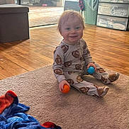 Oliver joined the competition — help win amazing prizes! toddler, child, pajamas, football_pattern, rug, floor, balls, smiling, indoors, blanket, storage_drawers, wooden_floor, toy, happy, person, home, living_room, casual, clothing, young_child