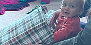 Oliver is registered to the contest to win money with this photo: toddler, child, gift_bag, plaid, indoor, carpet, adult_hand, chair, socks, person, smile, hair, floor, jeans, sitting, cozy, home, furniture, happy, curious
