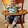 baby, balloon, birthday, cake, cake_smash, child, crumbs, dessert, frosting, hands, happy, high_chair, indoor, mess, onesie, portrait, smile, socks, toddler, wooden_chair