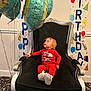 Oliver is registered to the contest to win money with this photo: balloons, birthday_banner, black_cushion, carpet, celebration, child, curious_expression, gift_party, hand_on_armrest, helium_balloons, indoor, looking_up, ornate_chair, party_decoration, red_hair, red_outfit, silver_frame, sitting, toddler, white_socks