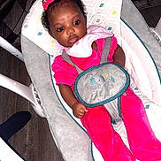 Alayah is registered to the contest to win money with this photo: baby, infant, child, pink_clothing, bow, baby_rocker, patterned_cushion, face, eyes, hand, footwear, indoors, wood_floor, seat_belt, cute, portrait, person, young_child, sitting, baby_girl