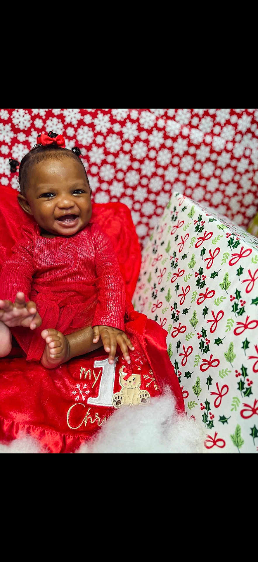 Alayah is registered to the contest to win money with this photo: baby, child, smiling, red_dress, holiday, christmas, festive, background, snowflakes, holly, gift_wrap, cute, happy, portrait, indoors, sitting, celebration, red_bow, infant, seasonal
