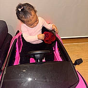 Christelle-Rose is registered to the contest to win money with this photo: black_pants, bouquet, child, gift, hair_bow, hardwood_floor, indoor, long_sleeve, looking_down, pink, playtime, portrait, present, roses, sitting, sofa, steering_wheel, toddler, toy_car, windshield