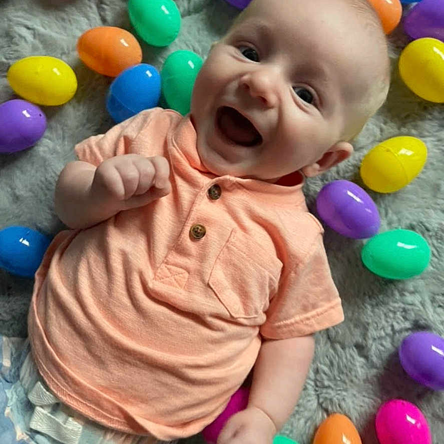 Rustyn is registered to the contest to win money with this photo: baby, blanket, bright_colors, celebration, child, colorful, cute, diaper, easter_eggs, happy, holiday, indoor, infant, lying_down, peach_shirt, plastic_eggs, playful, portrait, smiling, soft_texture