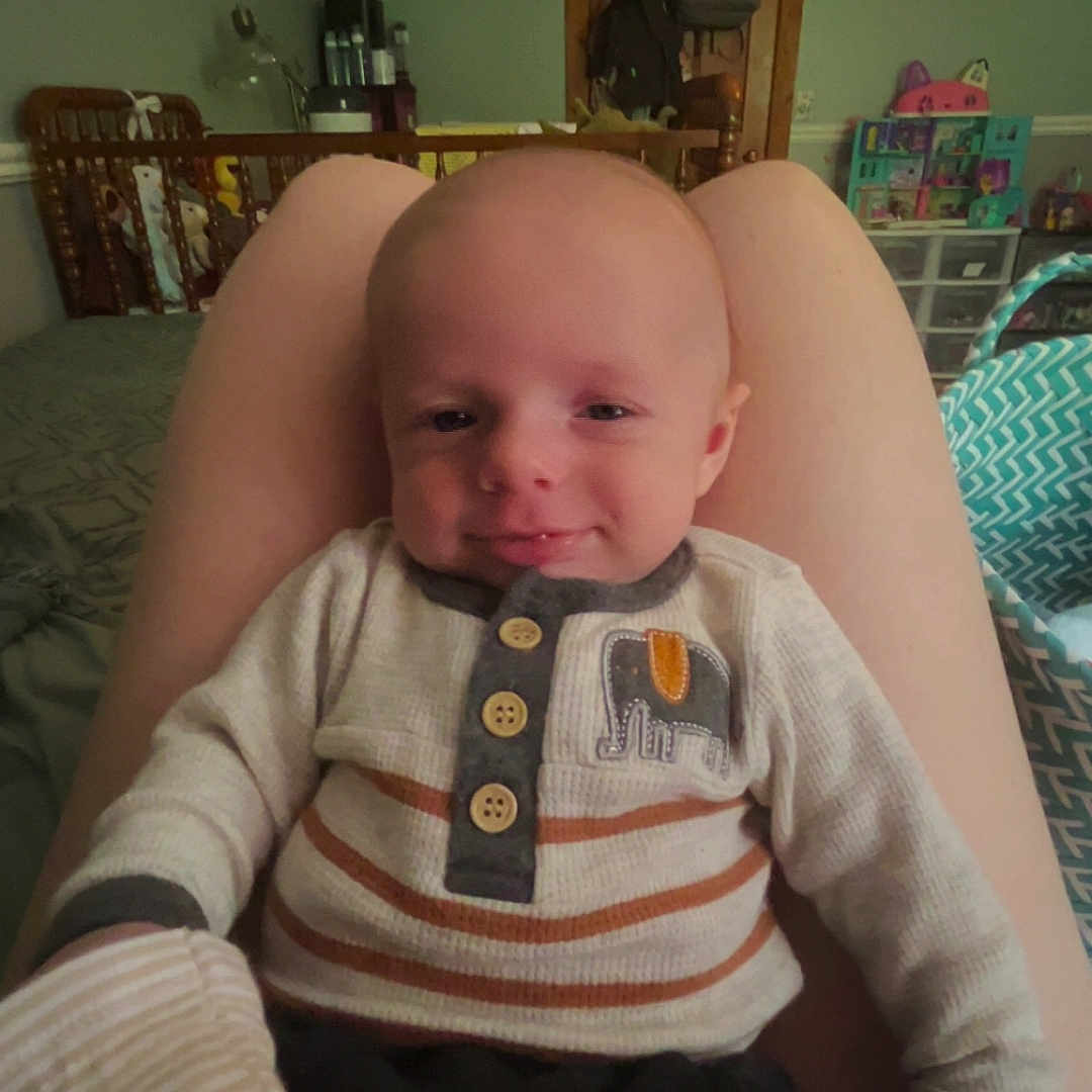 Oliver joined the competition — help win amazing prizes! baby, backpack, bedroom, blanket, child, comfort, door, elephant_patch, face, furniture, head, indoor, lap, person, smile, storage, striped_clothing, sweater, toy, wall