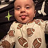 baby, infant, face, tongue, onesie, clothing, football, pattern, blanket, lying_down, cheeky, cute, smile, child, person, head, skin, indoors, sleepwear, expression
