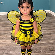 Carolina Vasquez joined the competition — help win amazing prizes! child, girl, bee_costume, yellow, black, antennae, wings, dress, tutu, striped_socks, striped_shoes, flowers, portrait, standing, indoors, wood_floor, blue_wall, costume, fashion, smiling