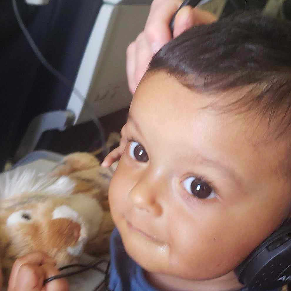 Noé participe au concours pour gagner de l'argent avec cette photo : airplane_seat, blue_shirt, cable, child, closeup, cute, expression, face, hair, hand, headphones, indoor, lion, person, playful, plush_toy, seat, toddler, travel, young_child