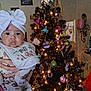 baby, bib, bow, child, christmas_tree, clothing, cute, decorations, face, festive, frame, hand, holiday, indoor, lights, ornaments, person, photograph, smile, wall