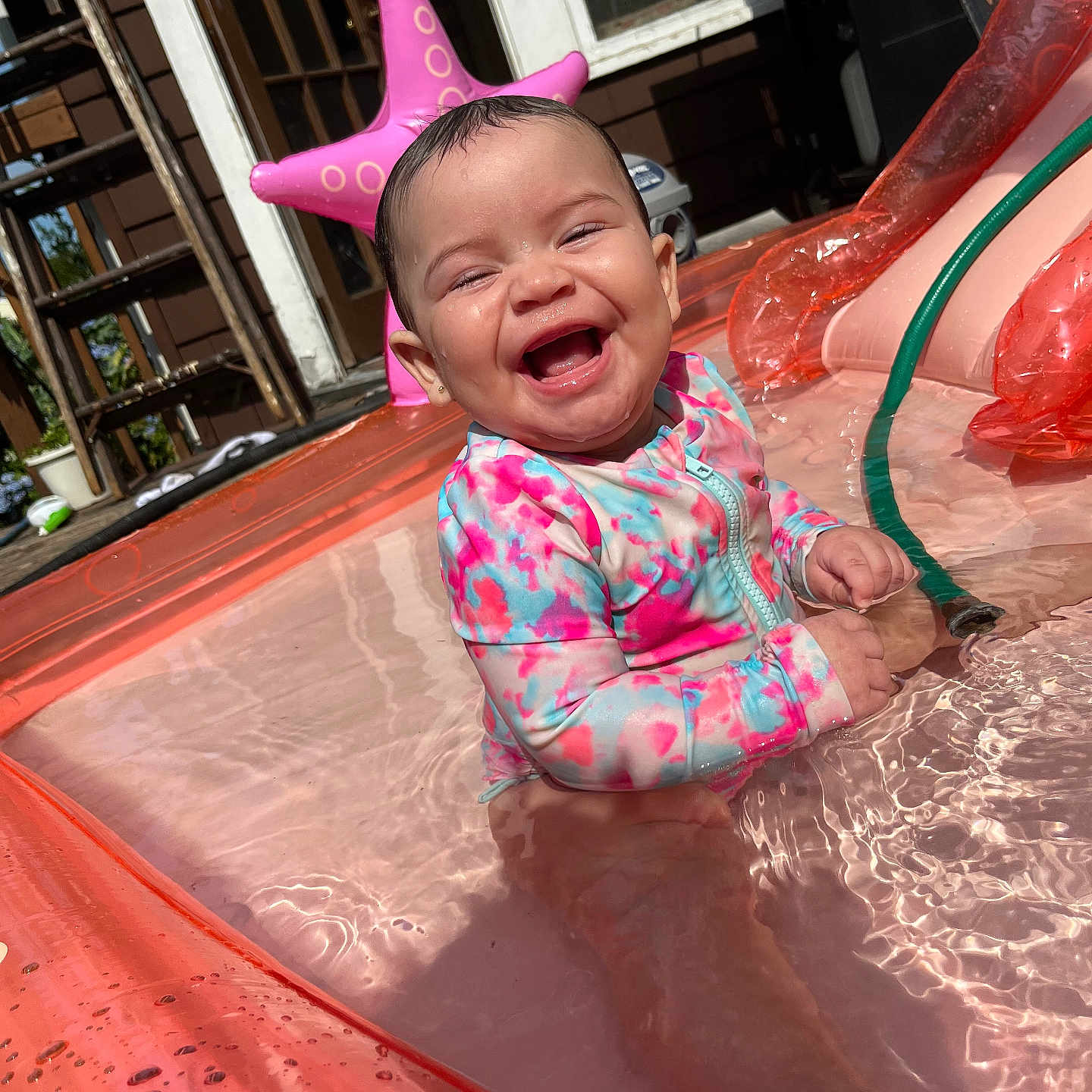 Adalaya is registered to the contest to win money with this photo: baby, child, infant, pool, water, swimsuit, inflatable_pool, smile, happy, outdoor, sunlight, starfish_float, hose, splash, play, summer, fun, joy, cute, sitting