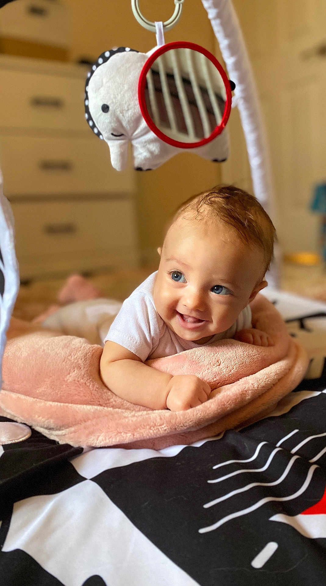 Kiara joined the competition — help win amazing prizes! baby, blue_eyes, smiling, blanket, plush_toy, elephant, mirror, soft_texture, indoor, child, cute, happy, infant, face, head, white_shirt, floor, play_gym, tummy_time, room