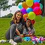 balloons, casual_clothing, child, colorful, daytime, fun, grass, greenery, happy, leisure, nature, outdoor, park, people, playful, roller_skates, sitting, smiling, tree, woman