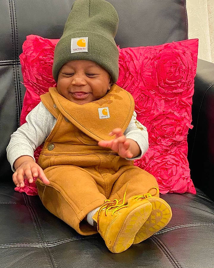 Gianni is registered to the contest to win money with this photo: baby, baby_toddler_clothing, beanie, cap, child, comfort, flooring, fun, head, headwear, human_body, human_leg, knee, knit_cap, lap, linens, magenta, outerwear, person, sitting