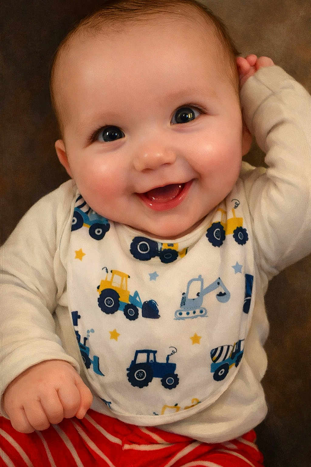 Jaxson is registered to the contest to win money with this photo: baby, infant, smiling, face, eyes, chubby_cheeks, bib, tractor_pattern, clothing, hand, portrait, closeup, indoor, happy, mouth, teeth, sleeve, striped_pants, skin, background
