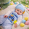 Jaxson is registered to the contest to win money with this photo: baby, infant, blue_hat, striped_overall, plush_toy, dinosaur, bunny_ears, easter_eggs, pastel_colors, flowers, cushion, soft_texture, smiling, holiday, celebration, spring, text_overlay, outdoor_background, child, portrait
