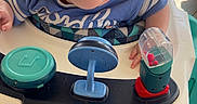Jaxson is registered to the contest to win money with this photo: baby, blue_shirt, child, closeup, curious, daylight, face, green_grass, high_chair, infant, outdoor, person, plastic_toy, playtime, porch, sitting, sunlight, toy, walker, young