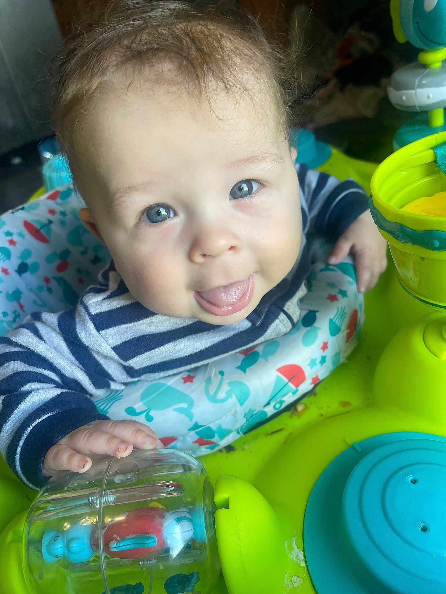 Milo is registered to the contest to win money with this photo: baby, child, toy, play_station, striped_shirt, blue_eyes, tongue_out, hand, face, smiling, indoor, colorful, plastic_toy, happy, infant, closeup, cute, person, young_child, playtime